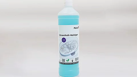 Blaufarbener Ultraschallreiniger in weißer Flasche mit Etikett vor grauem Hintergrund