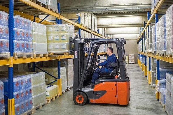 Gabelstapler transportiert palettierte Reinigungsprodukte im Hochregallager